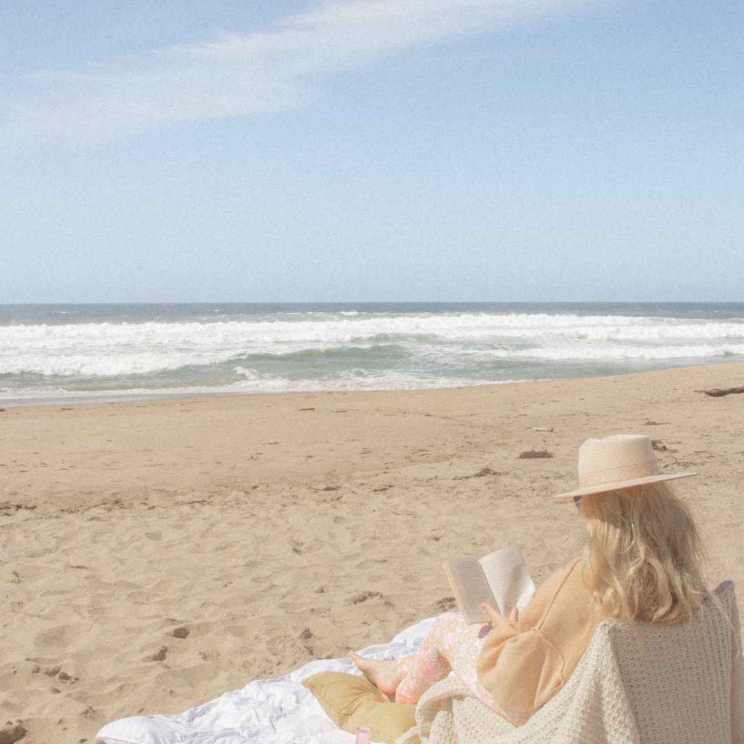 Woman reading on the beach wearing a hat