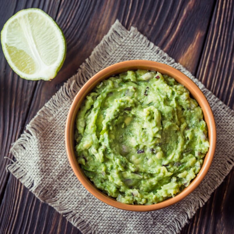 Bowl of green avocado dip on a wood table