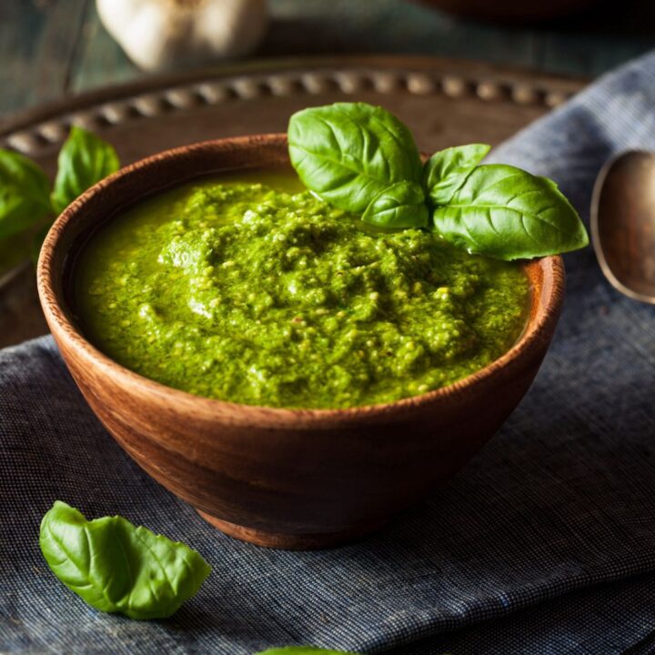 A wooden bowl filled with vibrant green vegan pesto sauce, garnished with fresh basil leaves, placed on a dark fabric napkin.