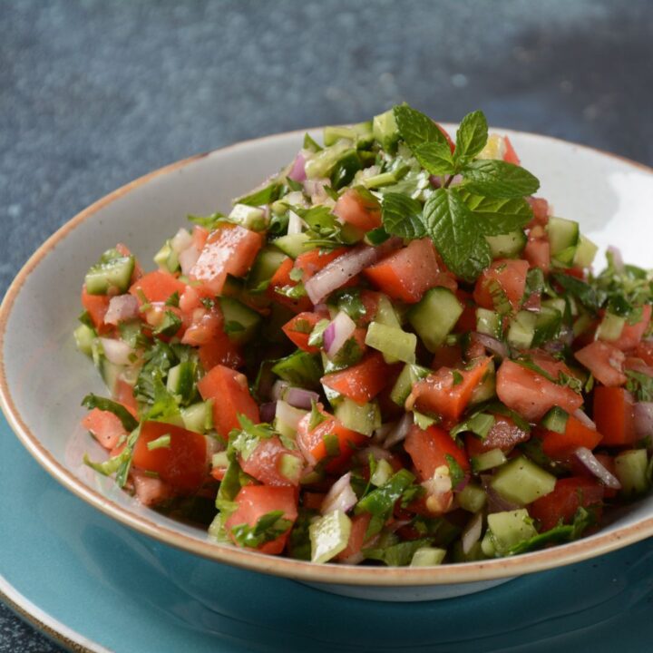 A bowl of diced tomatoes, cucumbers, onions, and herbs, garnished with a sprig of mint.